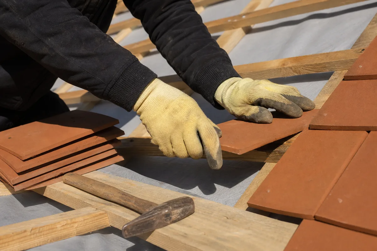 Mains d&rsquo;un couvreur posant des tuiles plates en terre cuite sur un liteaunage neuf